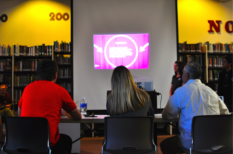 The 3 "sharks" of the shark tank judging students giving a presentation.